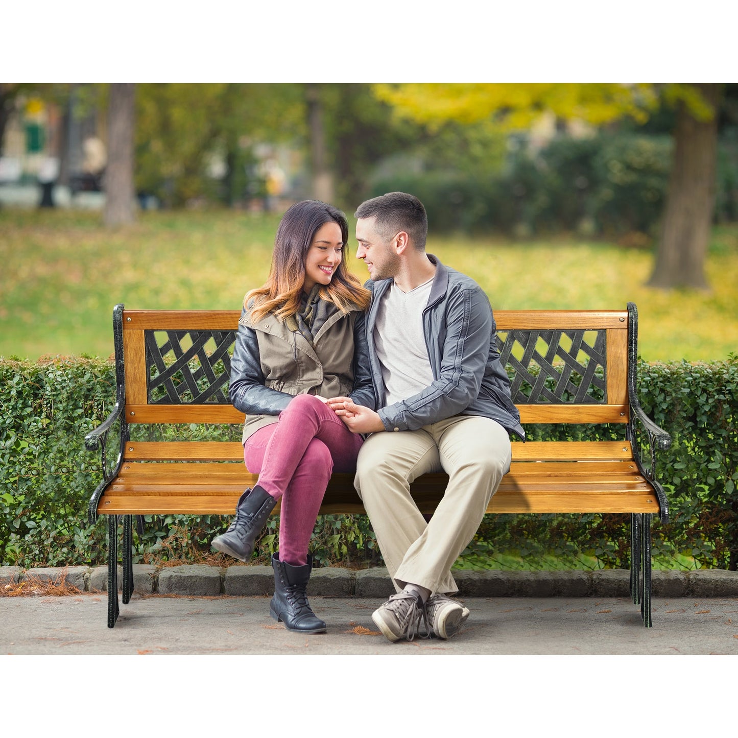 A couple sitting on a wooden bench with a metal frame and patterned backrest in a park setting.