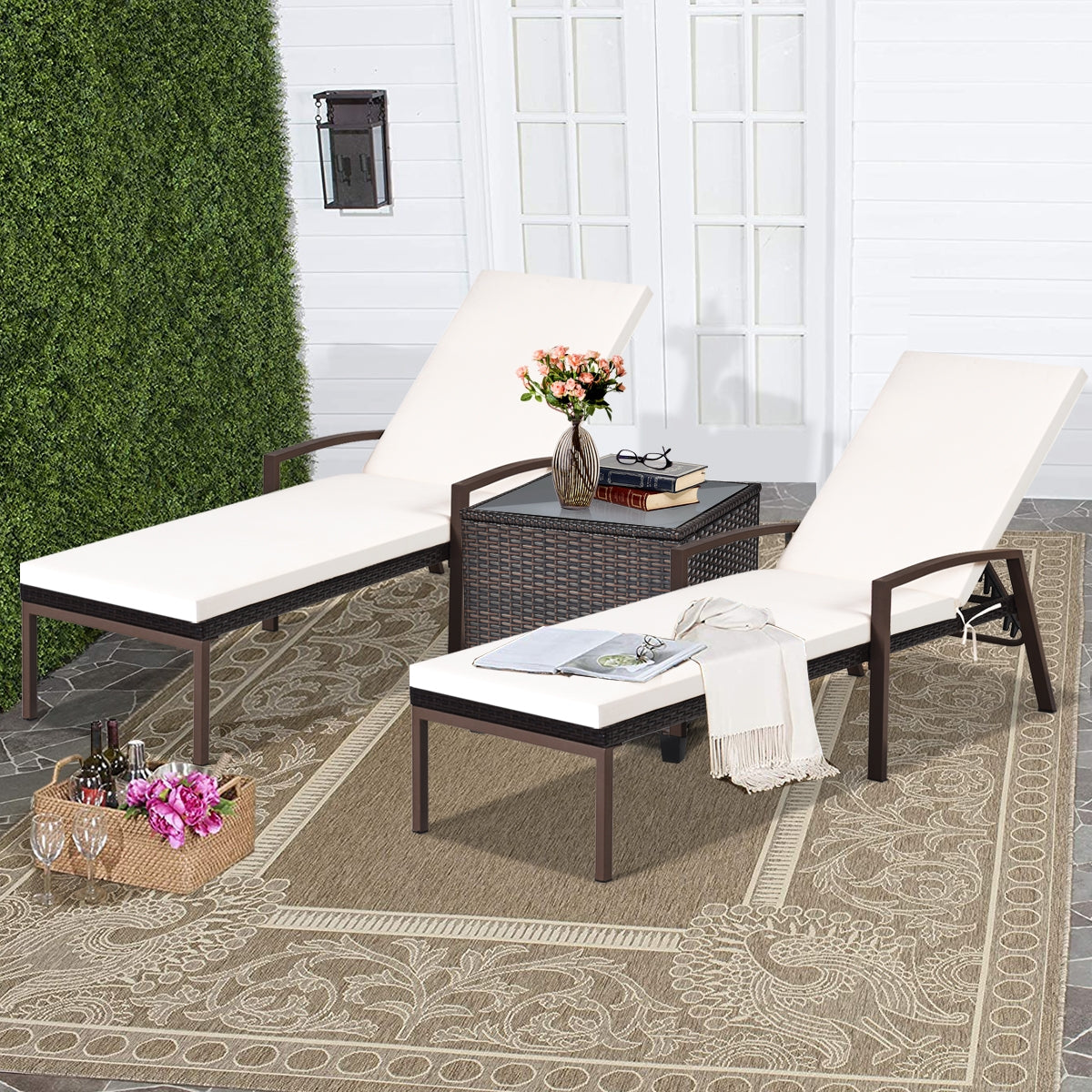 Two white cushioned patio rattan reclining chaise lounge chairs with armrests on a outdoor setting, featuring a small table between them with a vase of flowers on top.