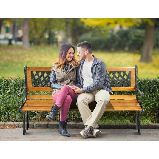 A couple sitting on a wooden bench with a metal frame and patterned backrest in a park setting.