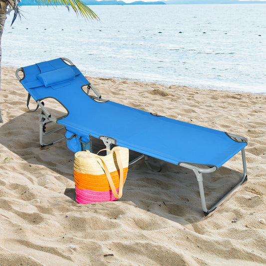 A blue folding beach lounge chair with a pillow, placed on a sandy beach with the ocean in the background.
