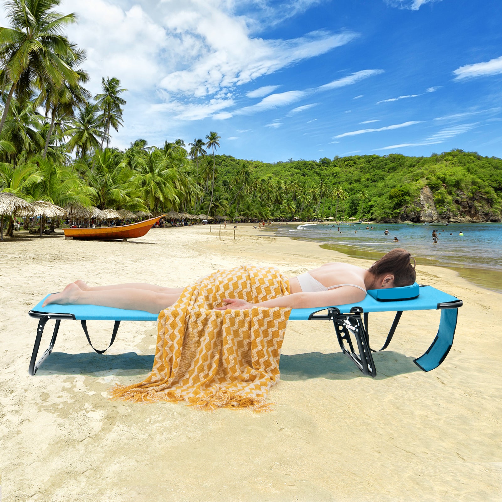 A person sunbathing on a blue beach chaise lounge chair with a face hole, located on a tropical beach with greenery and a boat in the background.