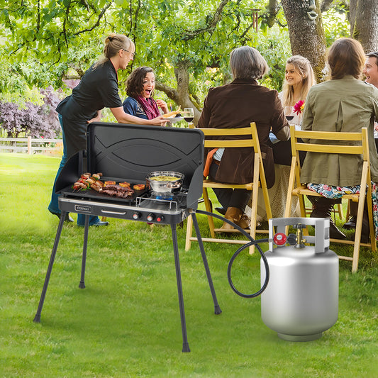 A black gas camping grill and stove with detachable legs, shown with people in the background indicating its use for outdoor cooking.