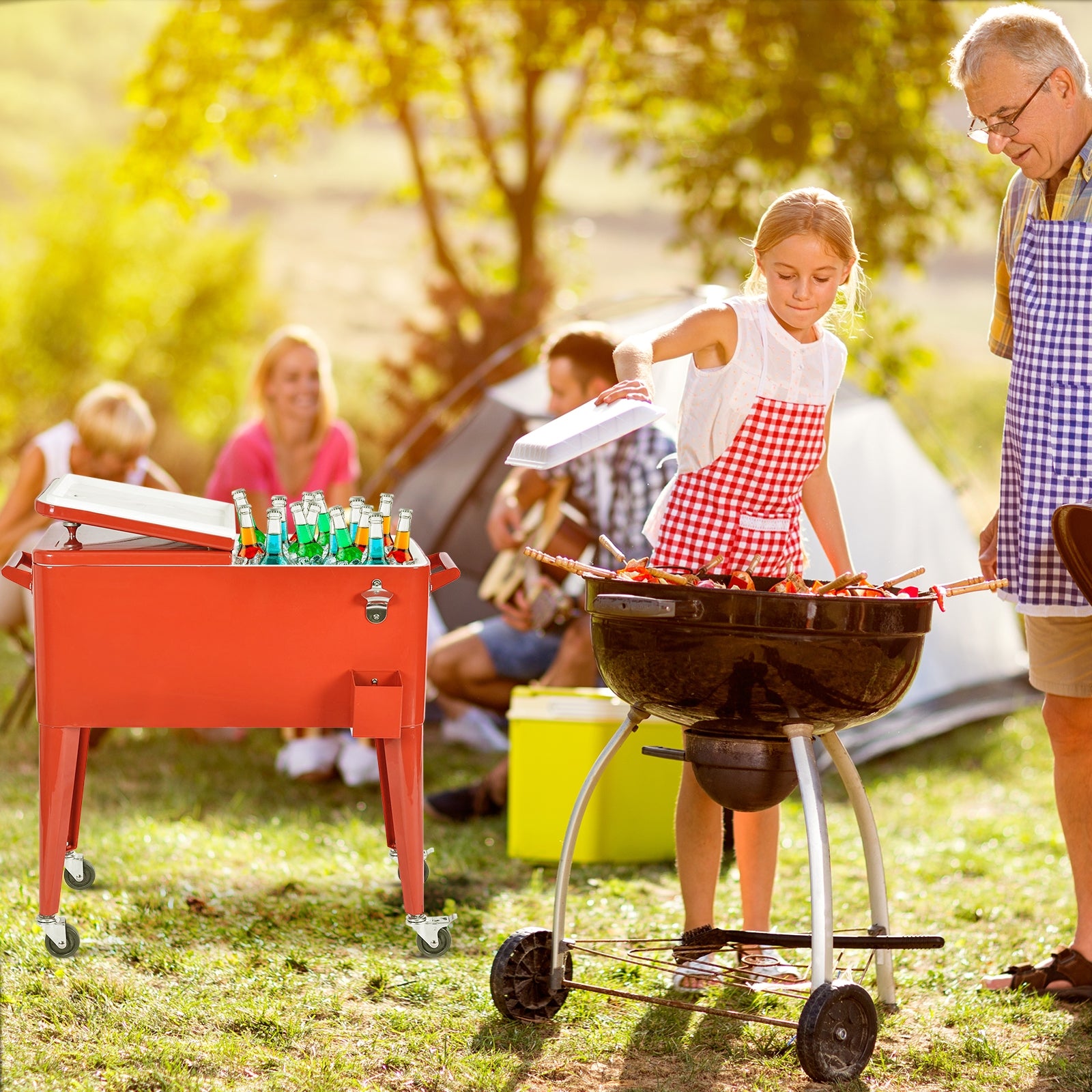 A red portable outdoor patio cooler cart with a child standing next to a man by a grill. Adults and children are enjoying outdoor activities in the background.