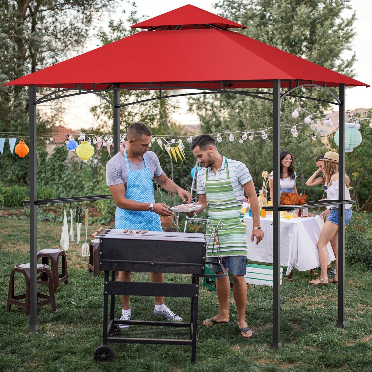 An outdoor barbecue grill gazebo with a red canopy, located in a garden setting with people gathered around the grill.