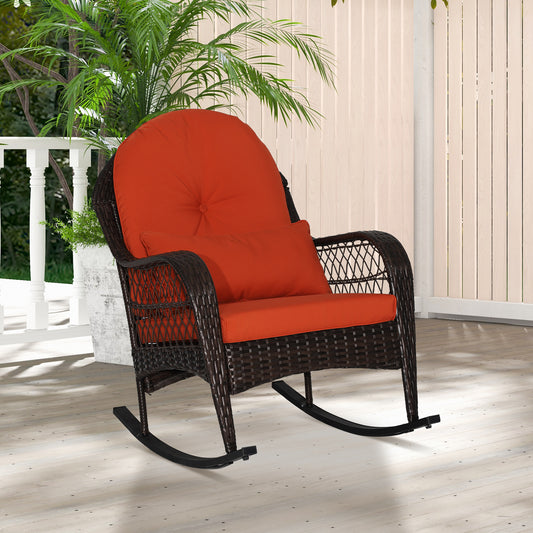 A red cushioned patio rocking chair made with a metal frame and PE rattan, displayed on a balcony with green plants in the background.