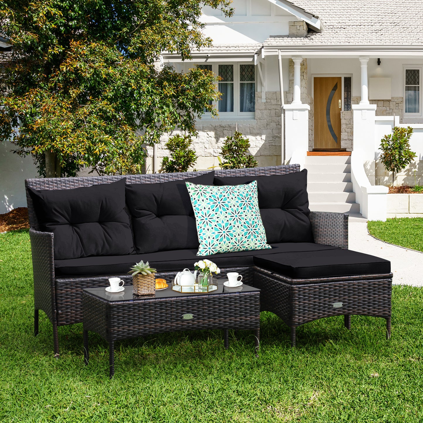 A black patio furniture set with a sectional sofa and a coffee table with a glass top, placed on a lawn in front of a house.