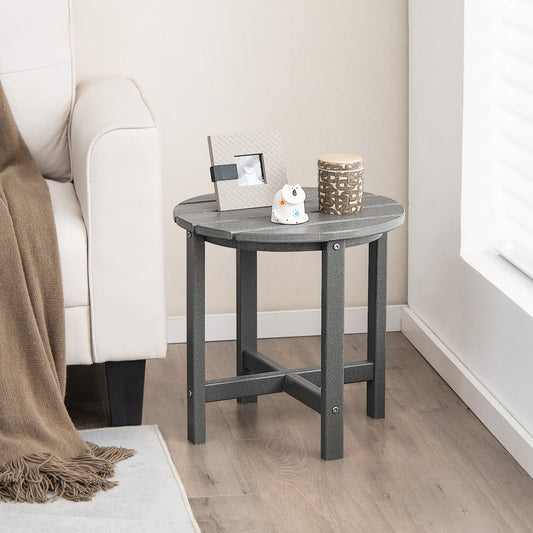 A gray round Adirondack side table made of HDPE with a slatted tabletop, placed next to a sofa with a decorative item and a remote on top.