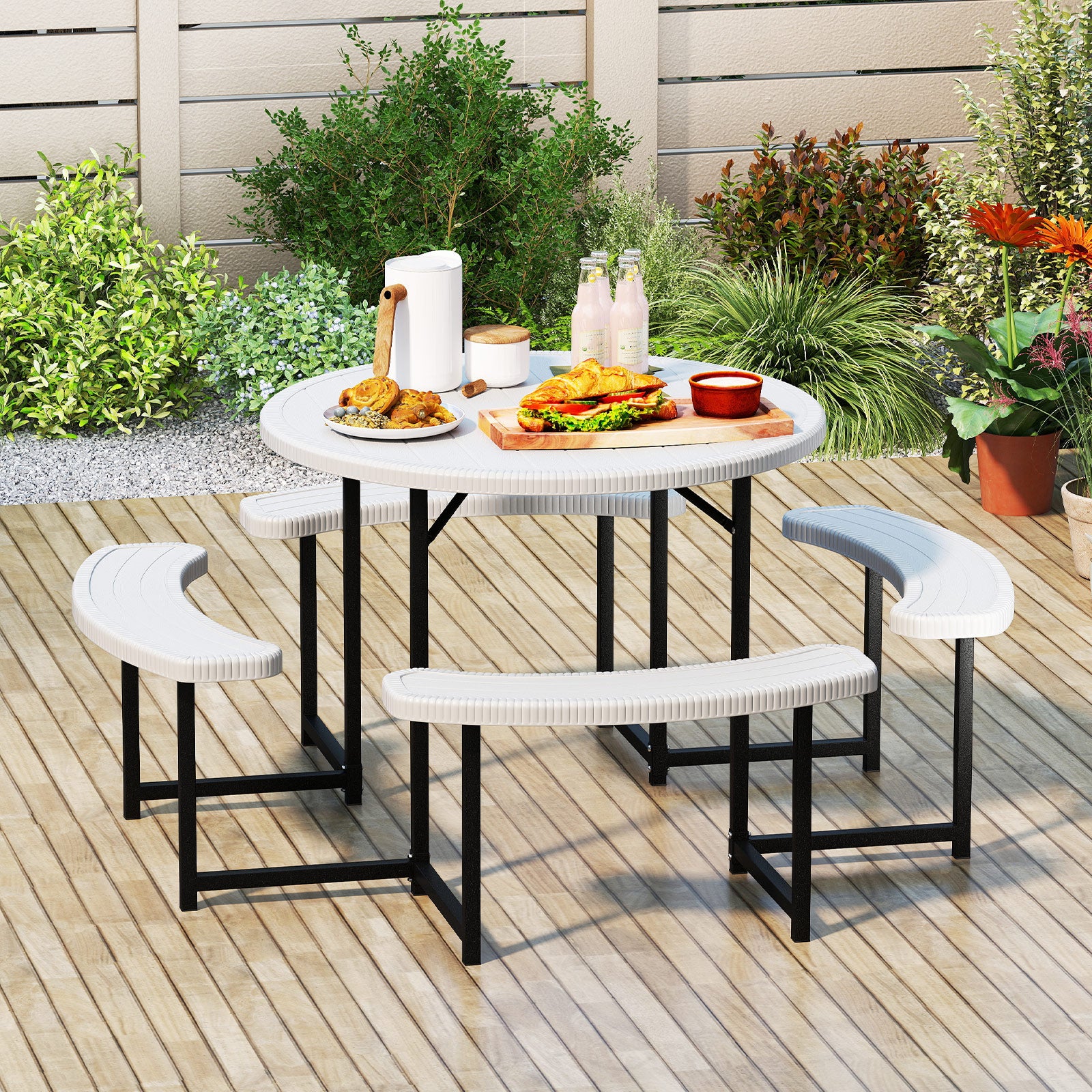 A round picnic table with a white HDPE tabletop and black metal legs, accompanied by four white curved benches with a faux shell texture. The set is placed on a wooden deck with outdoor seating and a small umbrella in the background.
