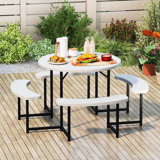 A round picnic table with a white HDPE tabletop and black metal legs, accompanied by four white curved benches with a faux shell texture. The set is placed on a wooden deck with outdoor seating and a small umbrella in the background.