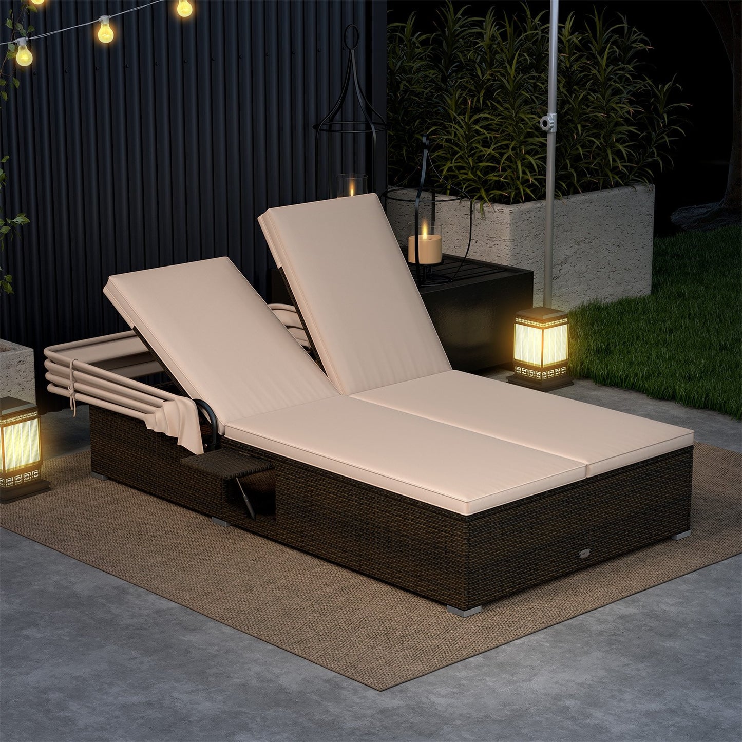 A beige patio double chaise lounge with shade cushions and folding side trays, placed on a outdoor setting with string lights and a candle in the background.