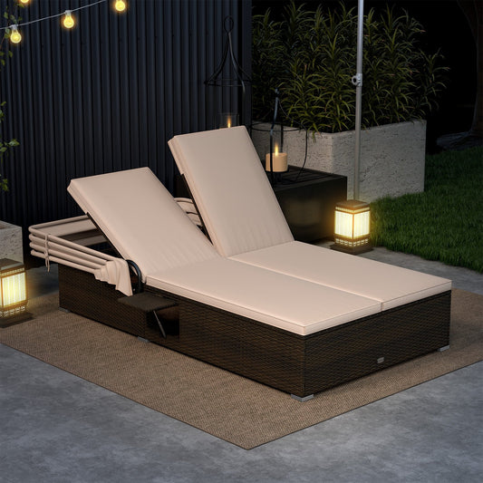 A beige patio double chaise lounge with shade cushions and folding side trays, placed on a outdoor setting with string lights and a candle in the background.