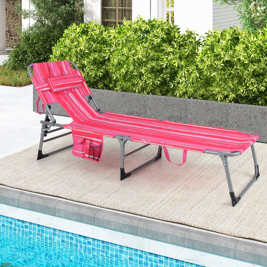 A folding beach lounge chair with a pink and white striped pattern, placed on a tiled area near a pool, with greenery in the background.