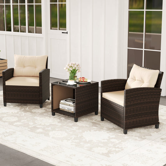 A three piece patio sofa set with two wicker chairs and a coffee table with a storage compartment. The set is beige and brown in color with cushions on the chairs and a book and a vase of flowers on the table, placed on a white rug.