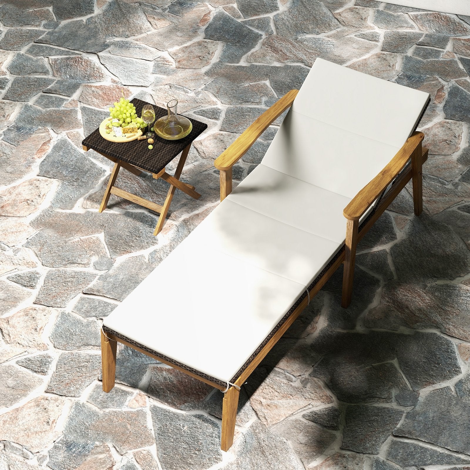 An outdoor chaise lounge chair with a white cushion and a folding coffee table next to it, both placed on a stone surface.