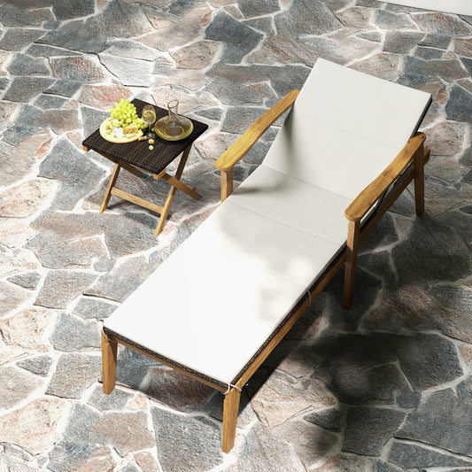 An outdoor chaise lounge chair with a white cushion and a folding coffee table next to it, both placed on a stone surface.