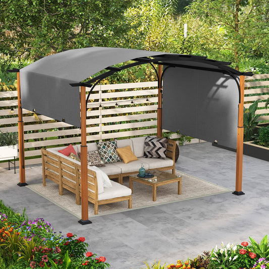 A gray outdoor retractable pergola with a retractable canopy installed on a patio, featuring a wooden-like surface on the posts and a gray fabric covering. There is outdoor furniture set arranged under it, consisting of a sofa and a coffee table, with a colorful garden in the background.
