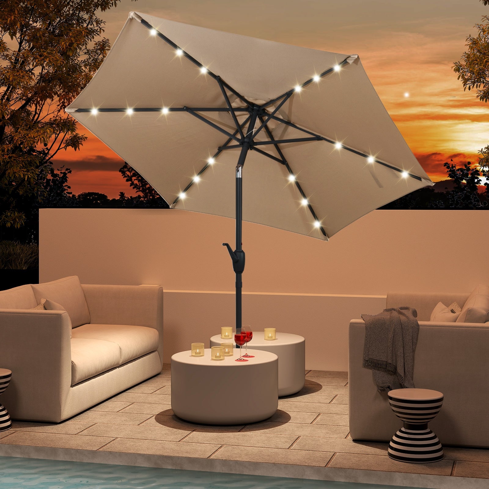 A beige patio umbrella with LED lights, featuring a crank handle, open and providing shade over an outdoor seating area at sunset.