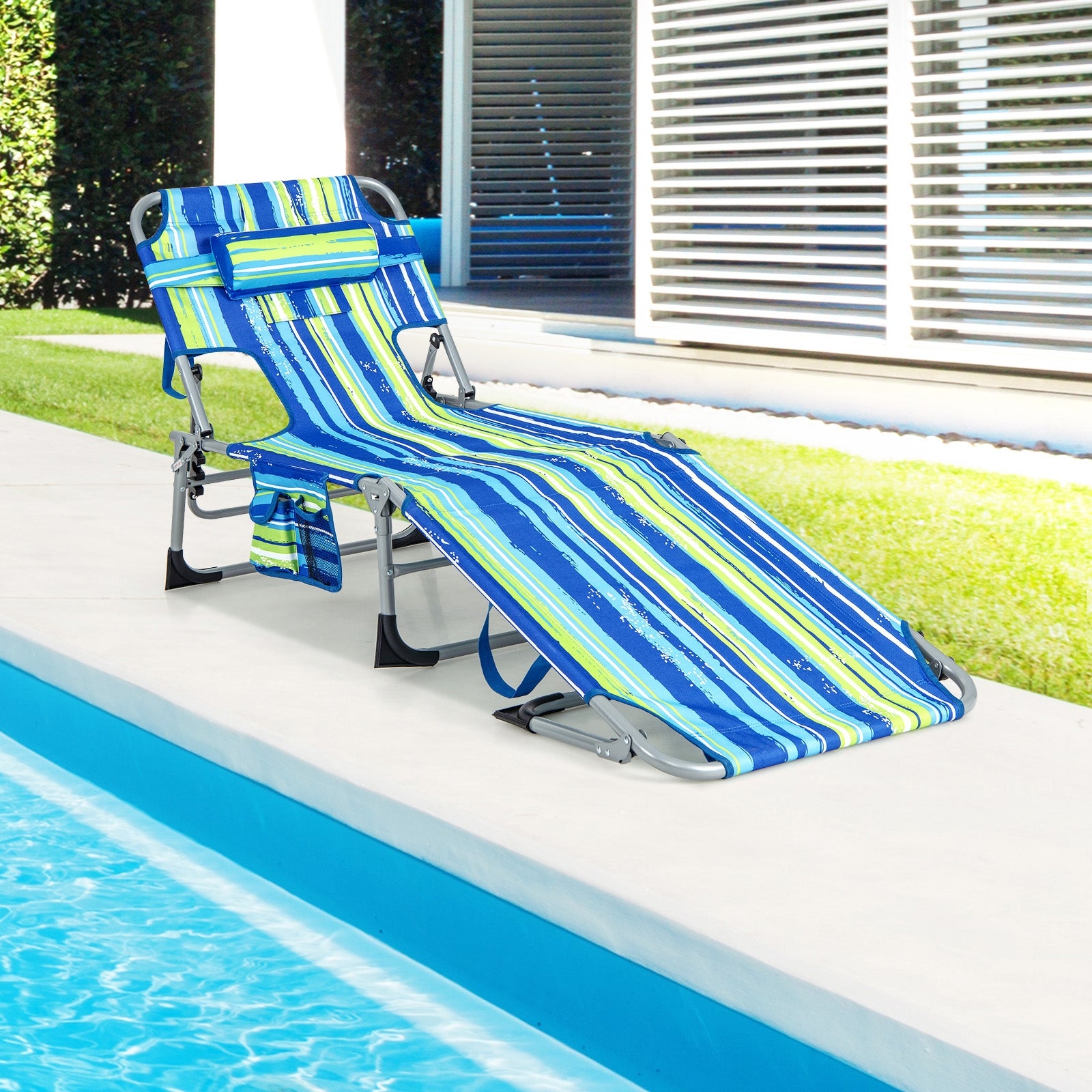 A folding beach lounge chair with a blue and green striped pattern, placed by a poolside.