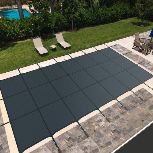 A blue safety pool cover installed on an in-ground swimming pool, surrounded by a stone deck with patio furniture in the background.